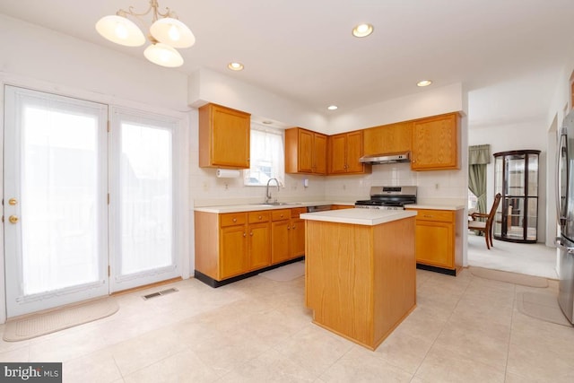 kitchen featuring sink, stainless steel stove, tasteful backsplash, a kitchen island, and decorative light fixtures