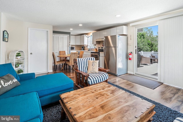 living room featuring a textured ceiling, sink, and light hardwood / wood-style floors