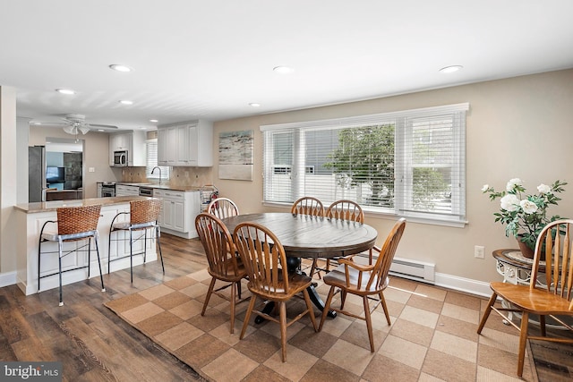 dining room with ceiling fan, light wood-type flooring, sink, and a baseboard heating unit