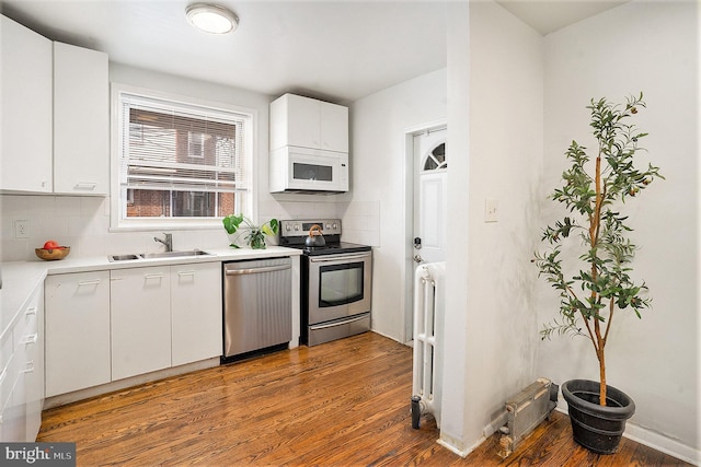 kitchen with sink, white cabinetry, backsplash, stainless steel appliances, and wood-type flooring