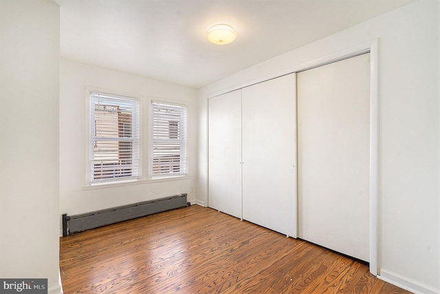 unfurnished bedroom featuring a baseboard radiator, hardwood / wood-style floors, and a closet