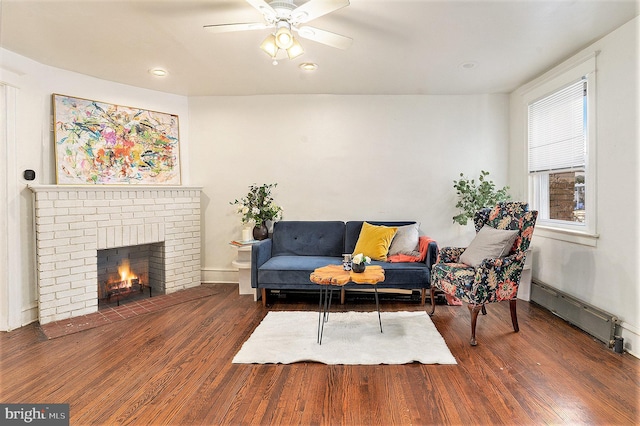 living room with a baseboard heating unit, ceiling fan, dark hardwood / wood-style floors, and a fireplace