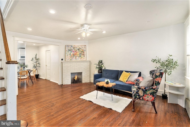 living room featuring a brick fireplace, dark hardwood / wood-style floors, and ceiling fan