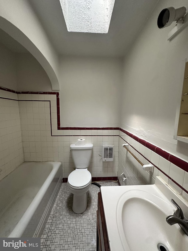 bathroom featuring tile walls, a tub to relax in, a skylight, vanity, and toilet