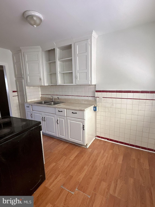 kitchen featuring tile walls, light hardwood / wood-style floors, white cabinetry, and sink