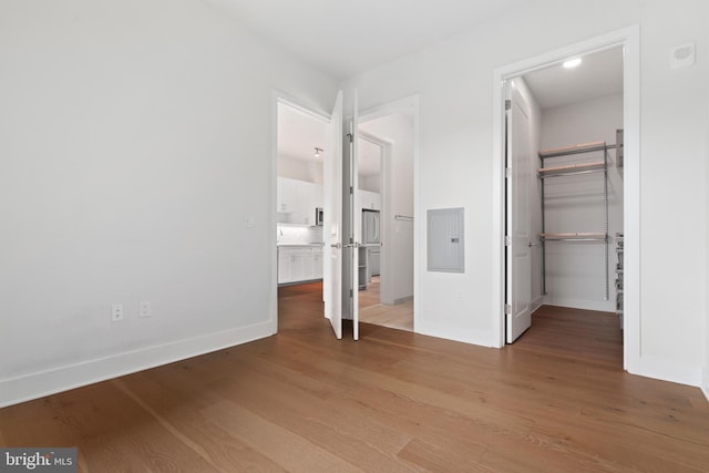 unfurnished bedroom featuring electric panel, wood-type flooring, a closet, a spacious closet, and ensuite bathroom