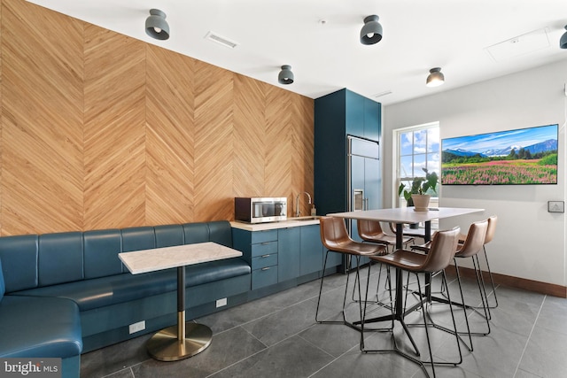 interior space with blue cabinetry, sink, wood walls, and dark tile patterned floors