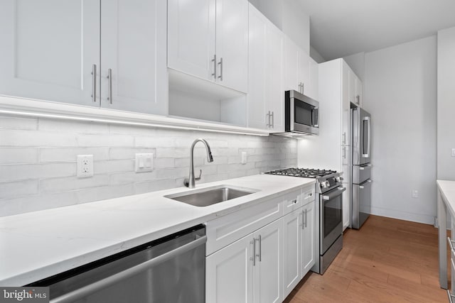 kitchen with sink, light hardwood / wood-style flooring, white cabinetry, appliances with stainless steel finishes, and light stone countertops