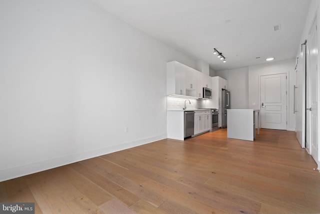 kitchen featuring white cabinetry, tasteful backsplash, stainless steel appliances, light wood-type flooring, and sink