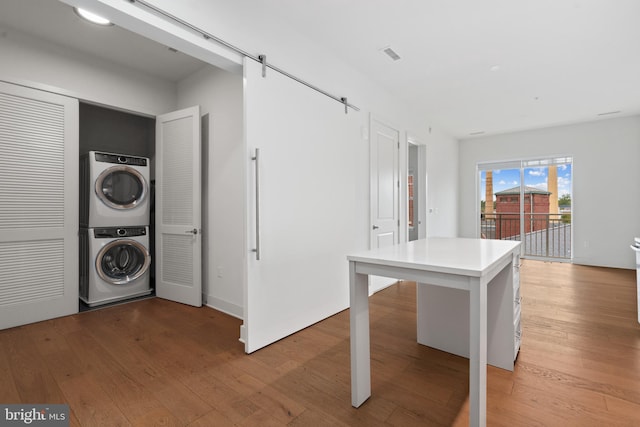 clothes washing area with stacked washer / dryer, a barn door, and light wood-type flooring