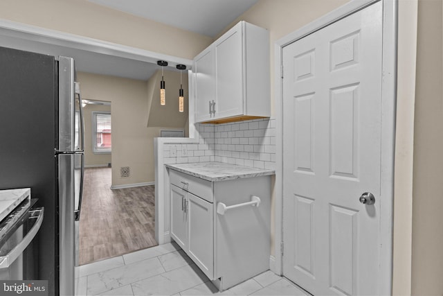 kitchen featuring stainless steel fridge, white cabinetry, light stone counters, backsplash, and pendant lighting