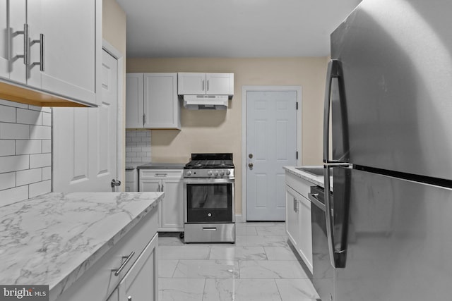 kitchen featuring appliances with stainless steel finishes, white cabinetry, light stone counters, and tasteful backsplash