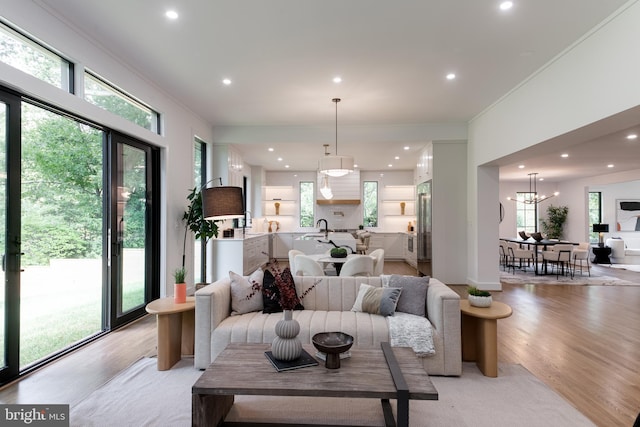 living room with a notable chandelier, light hardwood / wood-style floors, sink, and crown molding