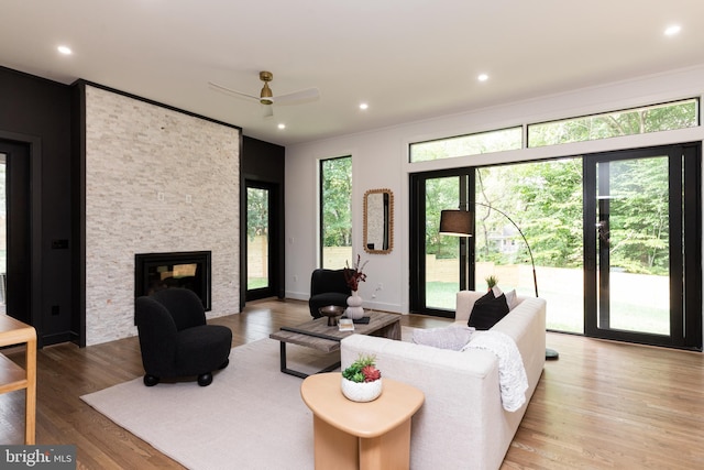 living room featuring ceiling fan, a stone fireplace, plenty of natural light, and light hardwood / wood-style floors