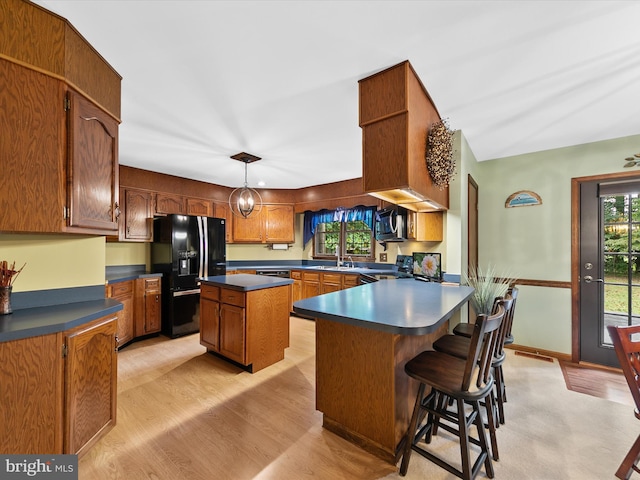 kitchen with a kitchen island, pendant lighting, light wood-type flooring, black appliances, and sink