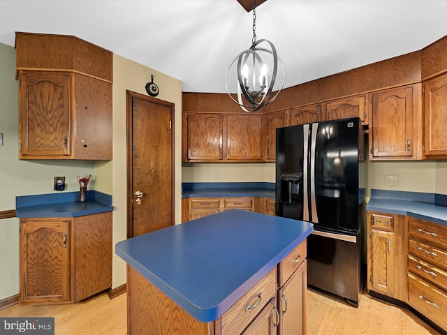 kitchen featuring light hardwood / wood-style floors, hanging light fixtures, a kitchen island, an inviting chandelier, and black fridge with ice dispenser