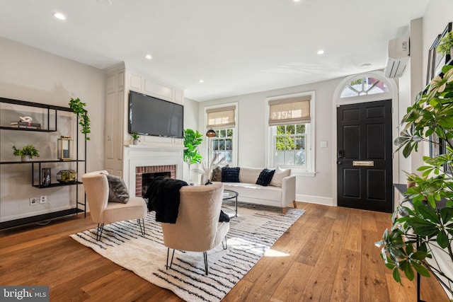 living room with a brick fireplace, hardwood / wood-style flooring, and a wall unit AC