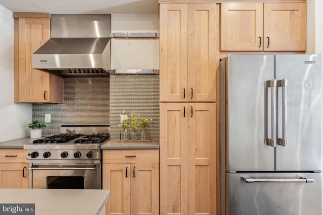 kitchen featuring light brown cabinetry, premium appliances, wall chimney exhaust hood, and decorative backsplash