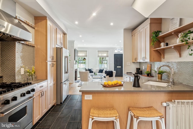 kitchen featuring light brown cabinets, ventilation hood, sink, kitchen peninsula, and high quality appliances