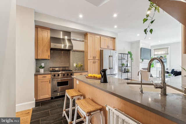 kitchen featuring light brown cabinets, premium appliances, dark wood-type flooring, wall chimney range hood, and a breakfast bar