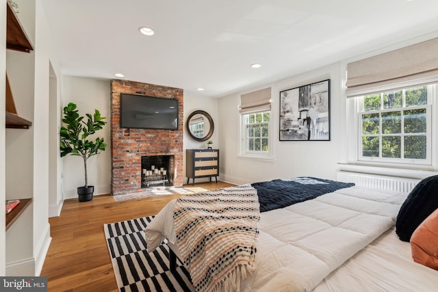 bedroom with a brick fireplace, radiator, and light hardwood / wood-style flooring