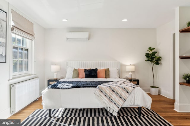 bedroom with radiator heating unit, a wall mounted AC, and light hardwood / wood-style flooring