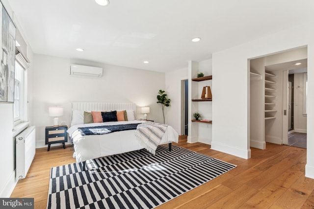 bedroom with radiator, light wood-type flooring, and a wall unit AC