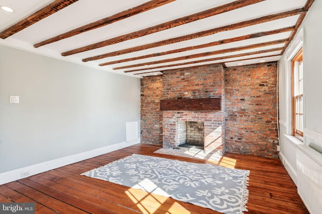 unfurnished living room featuring a brick fireplace, radiator heating unit, dark wood-type flooring, brick wall, and beam ceiling