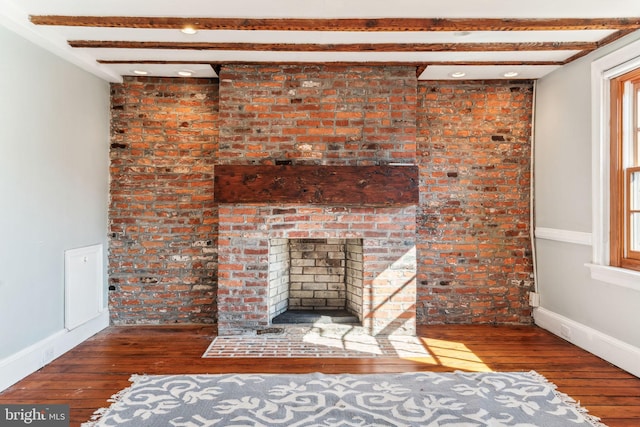 unfurnished living room featuring dark wood-type flooring, a brick fireplace, brick wall, and beam ceiling