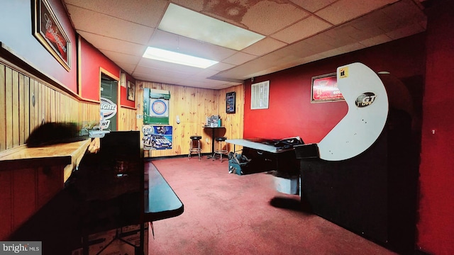 recreation room with a drop ceiling, wood walls, and carpet flooring