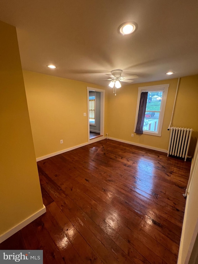 unfurnished room featuring plenty of natural light, dark wood-type flooring, ceiling fan, and radiator