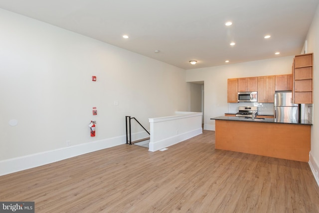 kitchen featuring appliances with stainless steel finishes, decorative backsplash, light hardwood / wood-style floors, kitchen peninsula, and sink