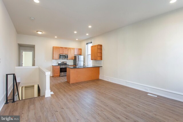 kitchen featuring light hardwood / wood-style flooring, stainless steel appliances, kitchen peninsula, and tasteful backsplash