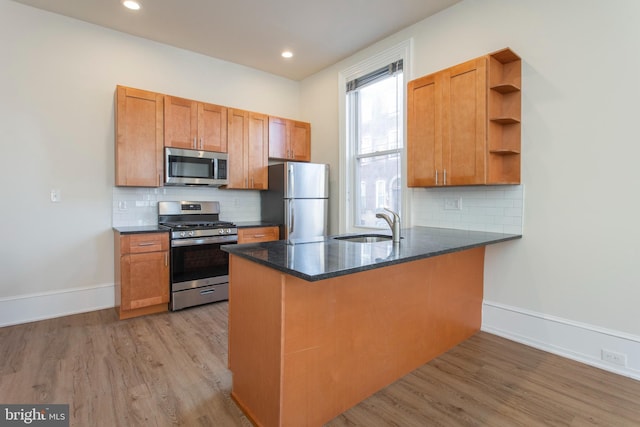 kitchen featuring appliances with stainless steel finishes, kitchen peninsula, light hardwood / wood-style floors, and tasteful backsplash