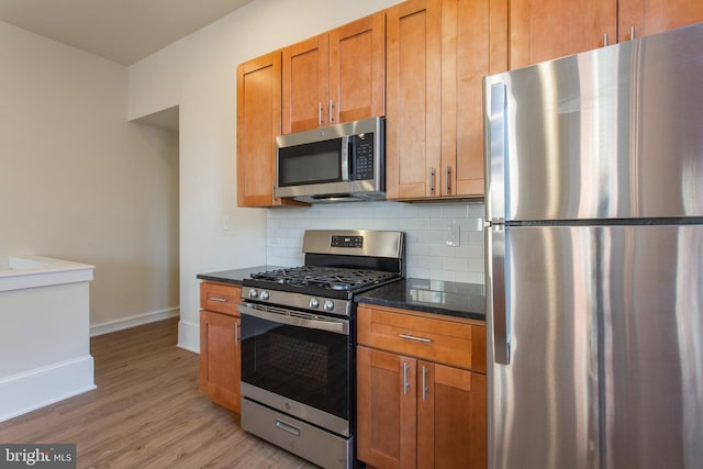 kitchen with decorative backsplash, light wood-type flooring, dark stone countertops, and appliances with stainless steel finishes