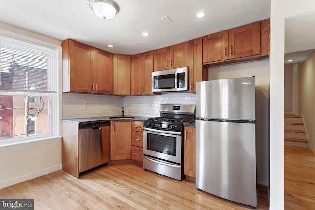 kitchen with sink, appliances with stainless steel finishes, light hardwood / wood-style floors, and tasteful backsplash