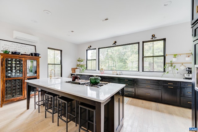 kitchen featuring an AC wall unit, light hardwood / wood-style floors, a center island with sink, and a kitchen bar