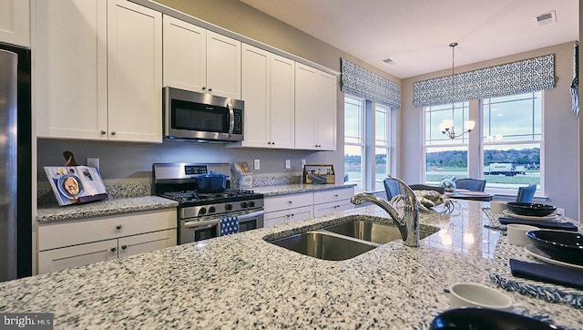 kitchen with sink, white cabinetry, appliances with stainless steel finishes, a notable chandelier, and light stone countertops