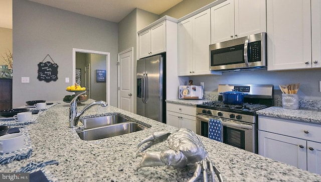 kitchen featuring light stone counters, stainless steel appliances, sink, and white cabinetry