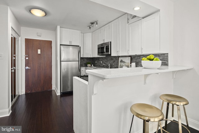 kitchen featuring dark wood-type flooring, white cabinets, kitchen peninsula, a kitchen breakfast bar, and stainless steel appliances