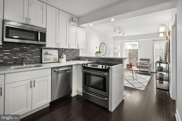 kitchen with sink, kitchen peninsula, white cabinetry, appliances with stainless steel finishes, and dark hardwood / wood-style floors