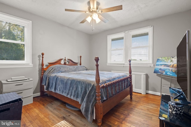 bedroom featuring radiator, hardwood / wood-style flooring, multiple windows, and ceiling fan