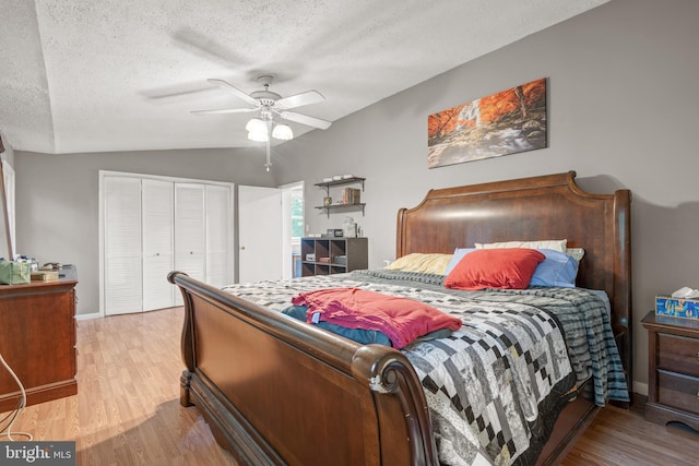 bedroom featuring light hardwood / wood-style floors, vaulted ceiling, a textured ceiling, and ceiling fan