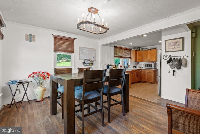 dining area featuring ornamental molding, dark wood-type flooring, a chandelier, and a textured ceiling