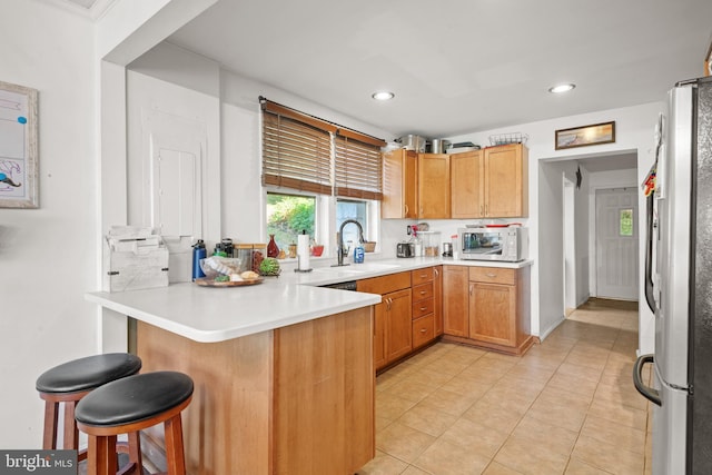 kitchen with sink, light tile patterned flooring, kitchen peninsula, appliances with stainless steel finishes, and a kitchen bar