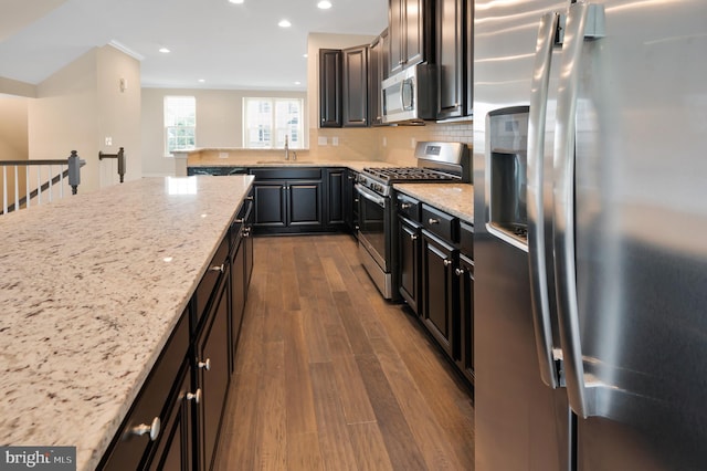 kitchen with light stone counters, sink, backsplash, appliances with stainless steel finishes, and dark hardwood / wood-style flooring