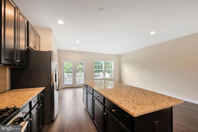 kitchen with dark wood-type flooring, light stone counters, a kitchen island, and tasteful backsplash