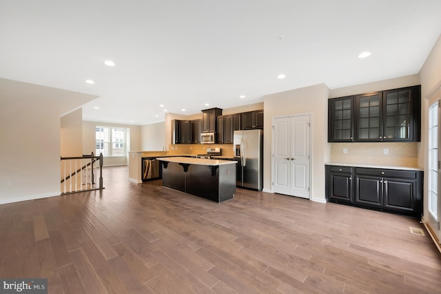 kitchen with appliances with stainless steel finishes, light hardwood / wood-style floors, a kitchen island, a kitchen bar, and dark brown cabinets