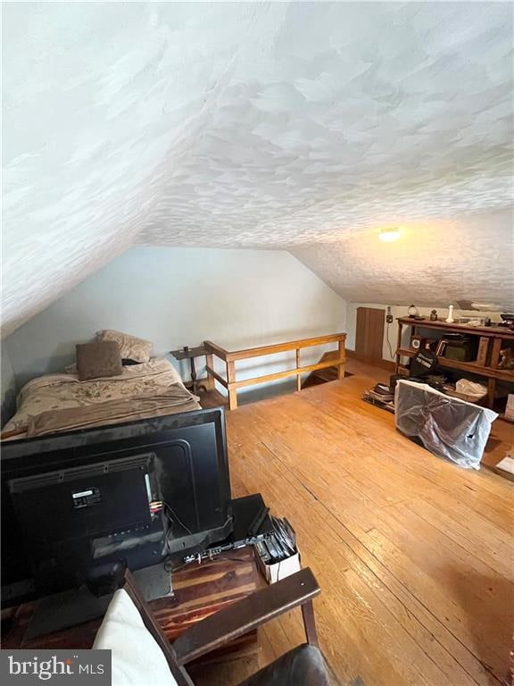 interior space with vaulted ceiling, a textured ceiling, and hardwood / wood-style flooring