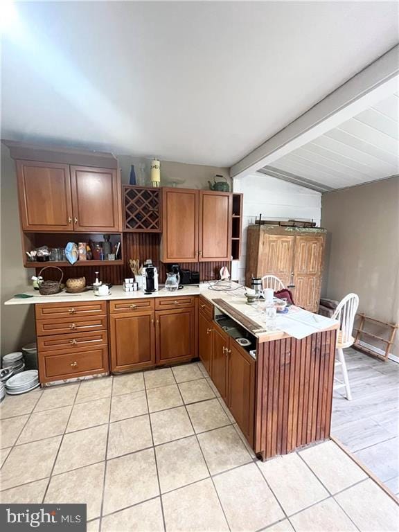 kitchen featuring kitchen peninsula, light tile patterned flooring, and beamed ceiling